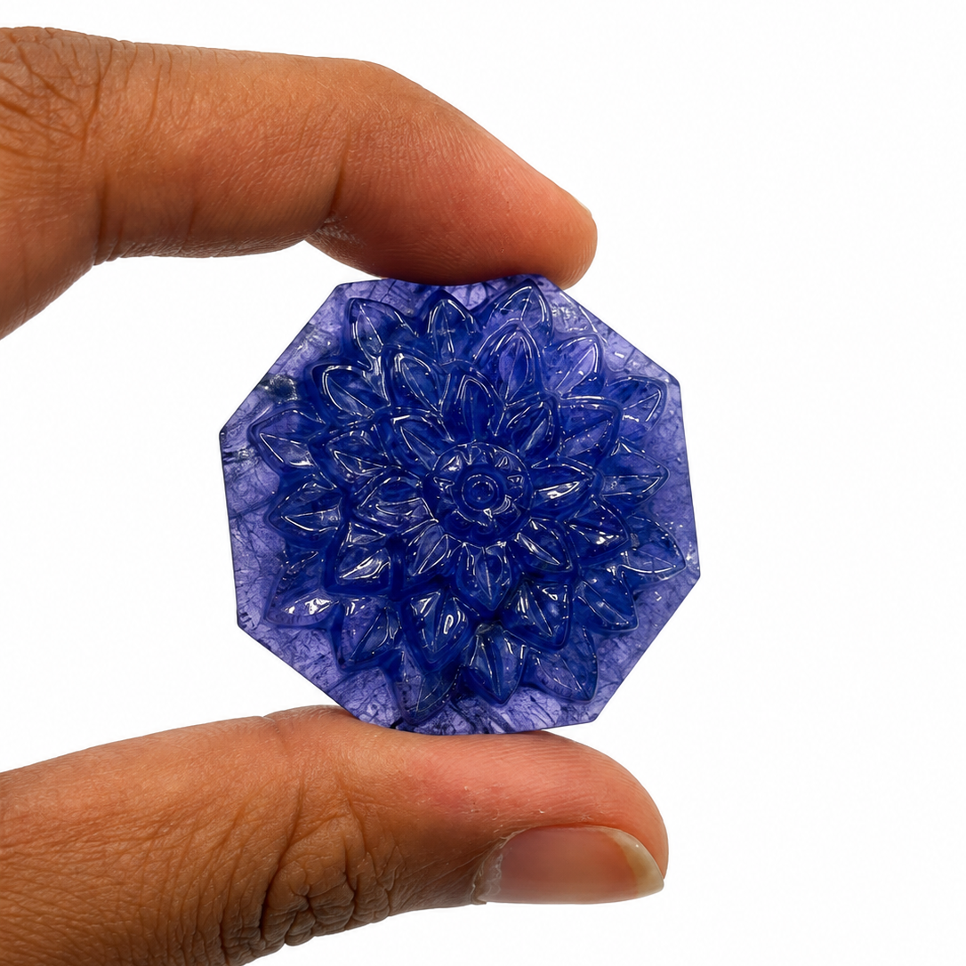 Carved tanzanite lotus tablet, 102 carats, held between fingers for scale