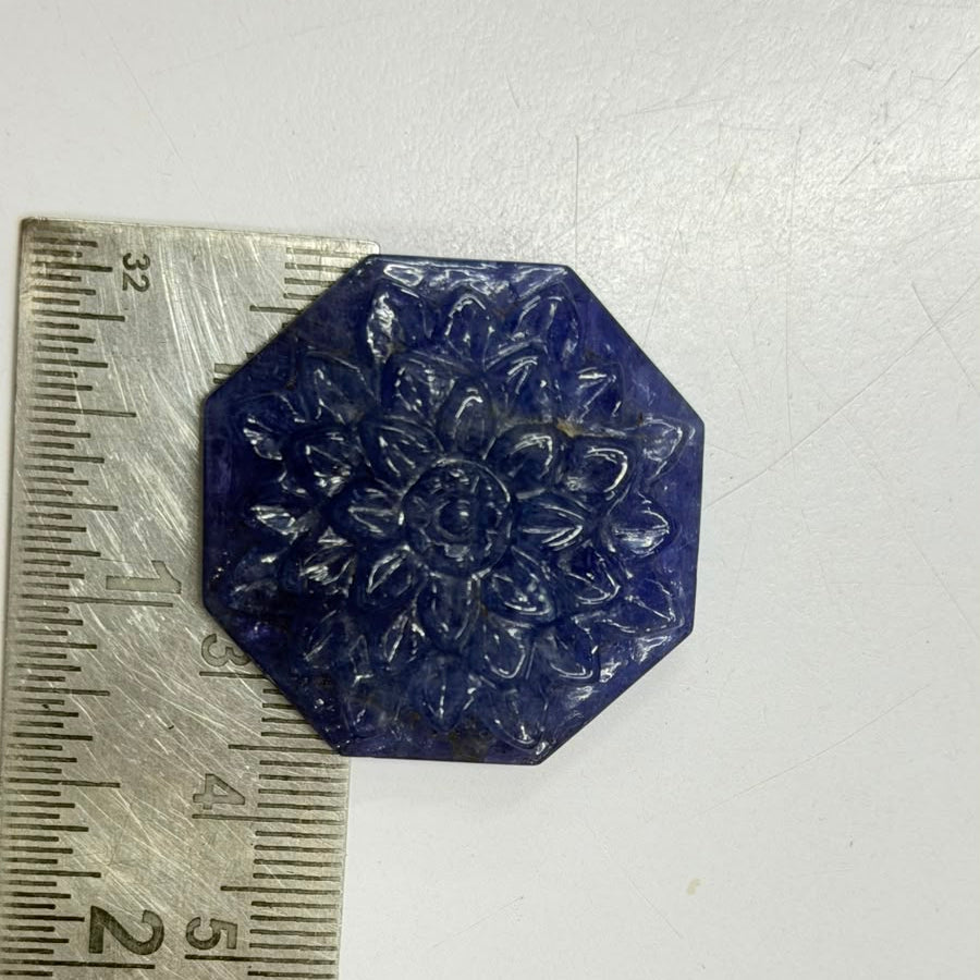Carved tanzanite lotus tablet measured against a ruler, approximately 3 cm across
